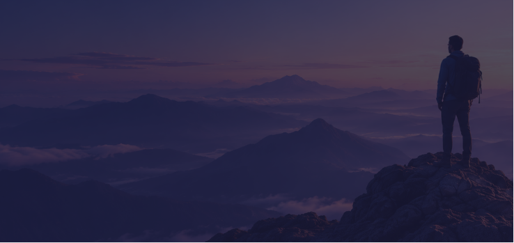 Silhouette of a hiker looking out over a misty mountain range at dusk
